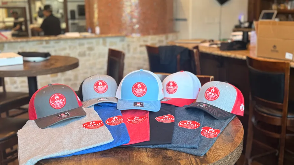 Cavalli Pizzeria hats and t-shirts displayed on a table inside the restaurant